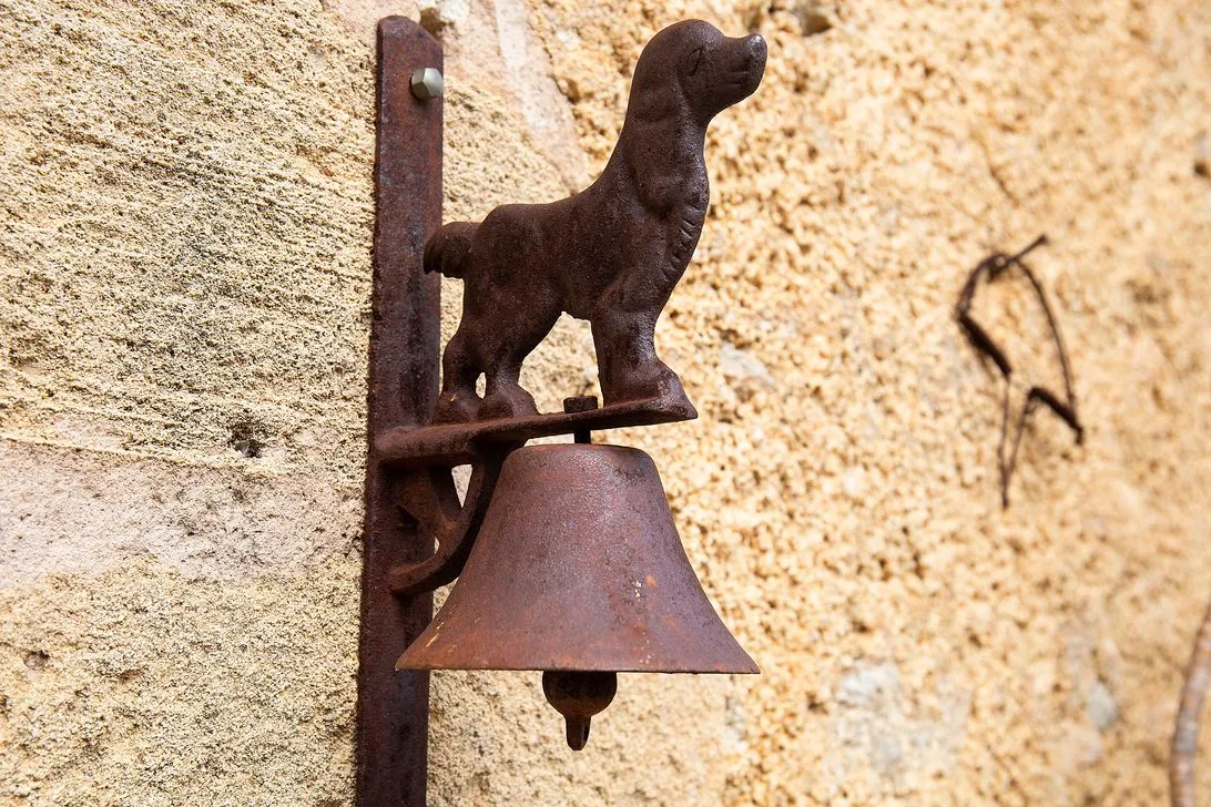A rusted dog-shaped bell mounted on the textured stone wall