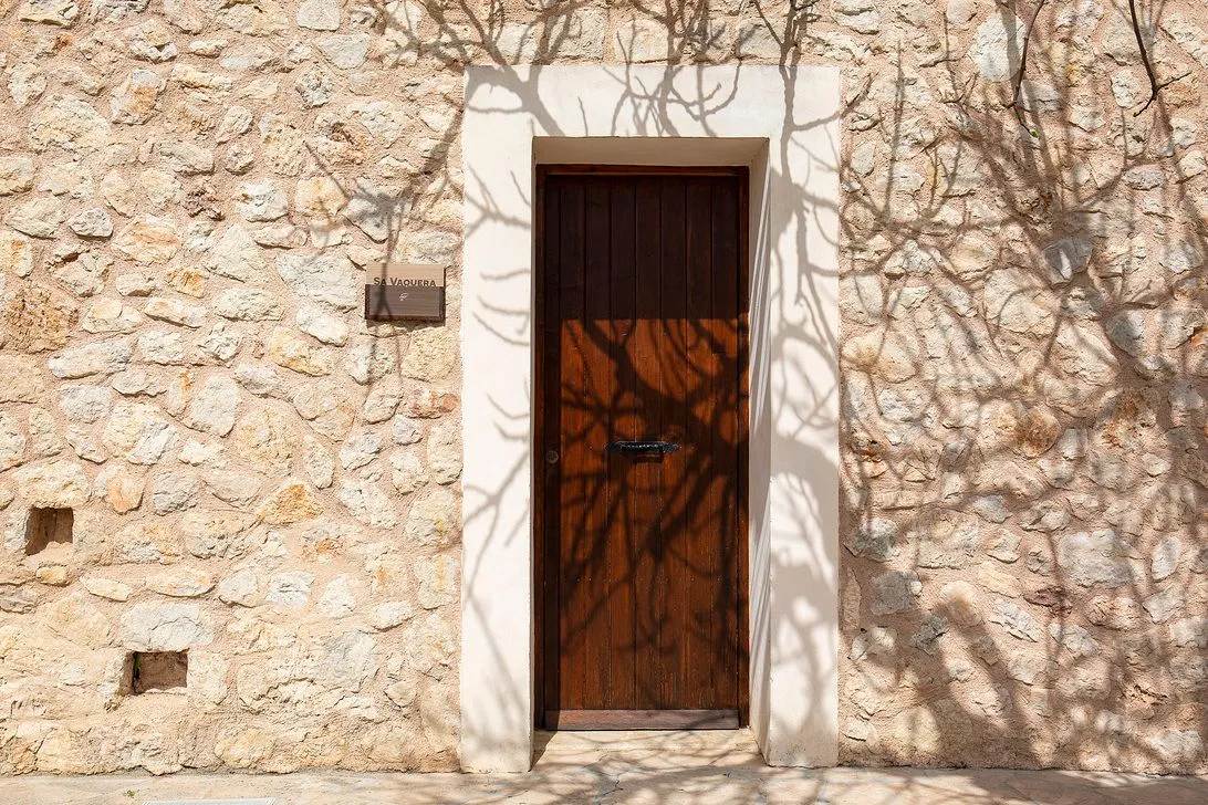A weathered wooden door set in the stone wall, under the shade of a tree