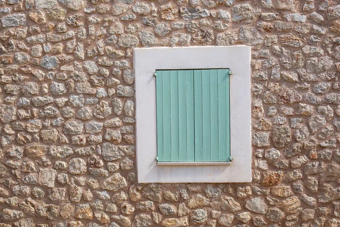 A window with teal-green shutters set in a white frame
