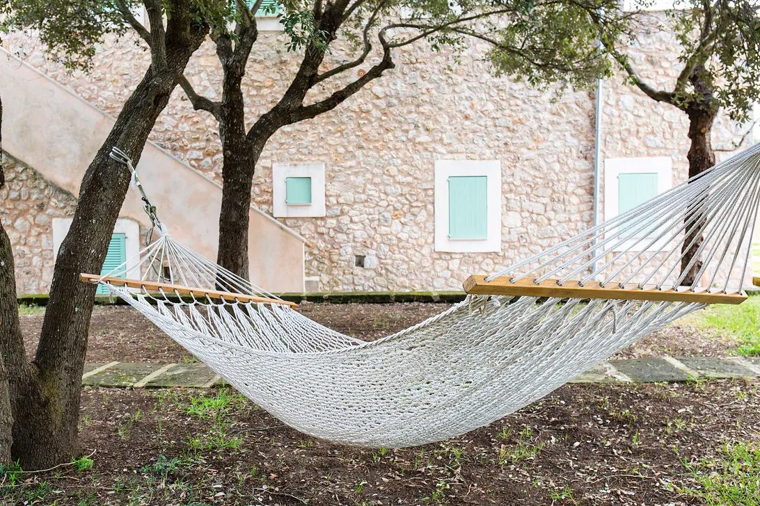 A hammock slung between two trees on the lawn before the stone building