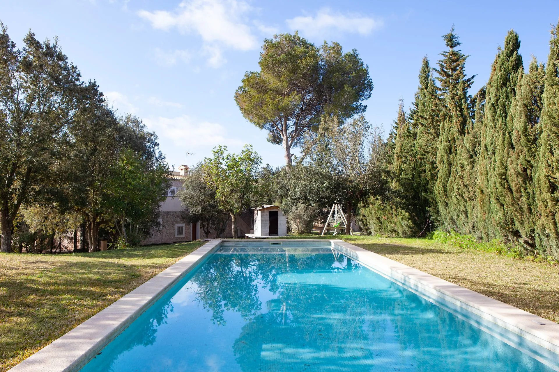The pool set in grass and trees, the stone house behind